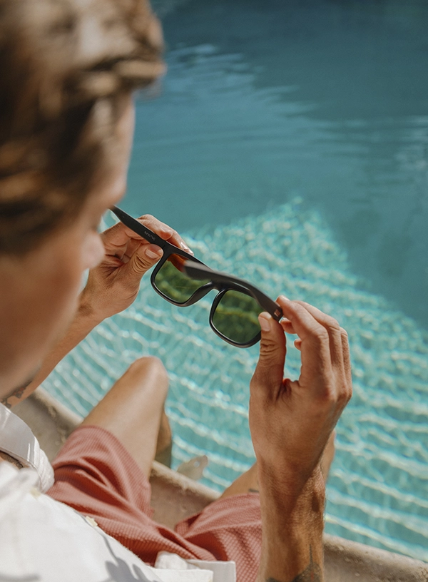 Bărbat lângă piscină punându-și ochelarii de soare